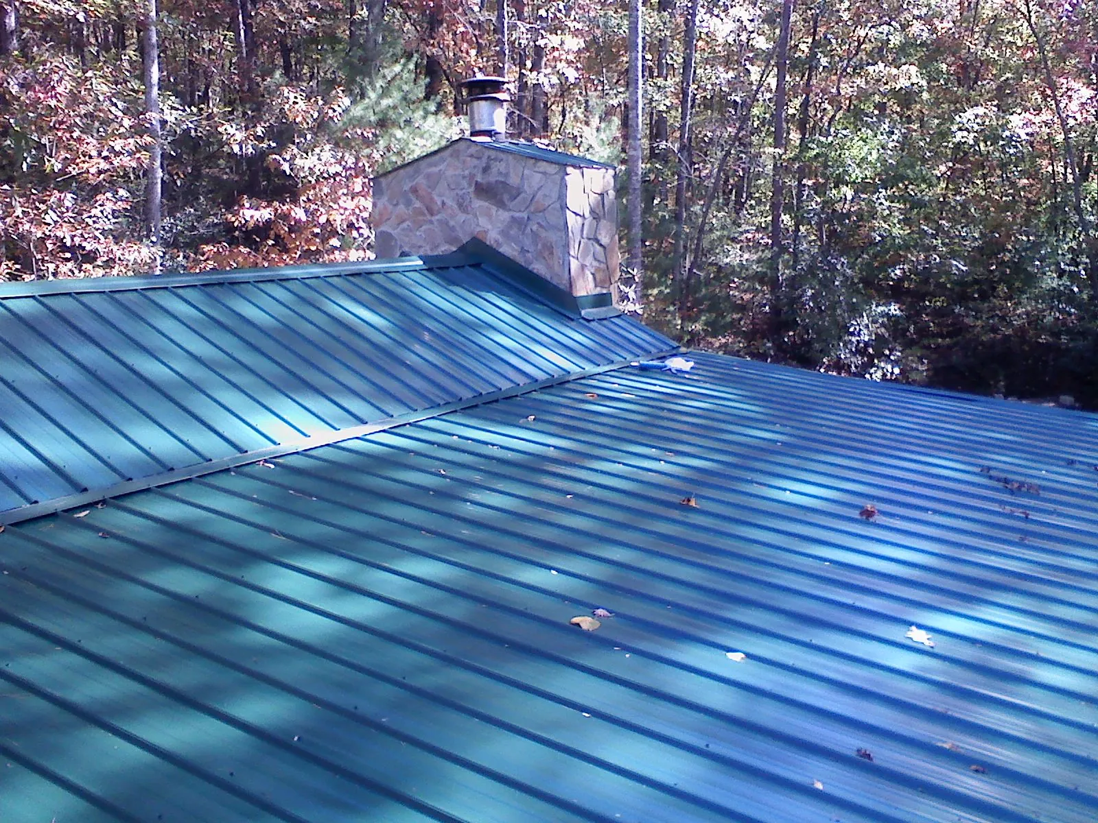 New green metal roof and stone chimney surrounded by autumn woods in Hawthorne